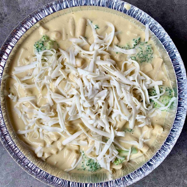 Real Fake Meats White Cheddah Penne with broccoli and white sauce in a round foil tray